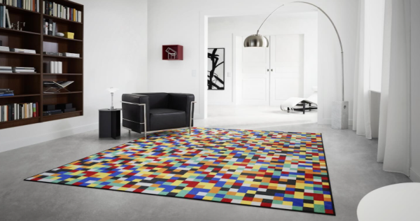 „Modernes Wohnzimmer mit farbenfrohem Vorwerk Teppich im Pixelmuster aus roten, blauen, gelben, grünen, schwarzen und weißen Quadraten; umgeben von minimalistischer Einrichtung mit schwarzem Sessel, weißer Lampe und Bücherregal.“